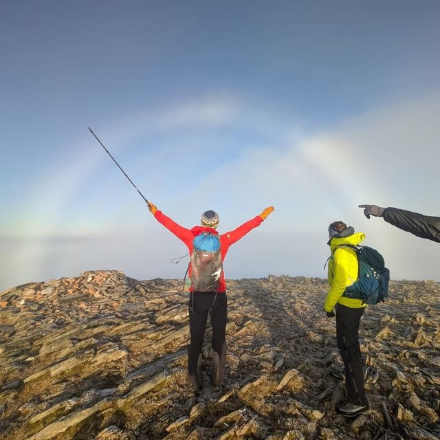 Arms and walking pole raised in celebration on a Munro summit beneath a Brocken spectre