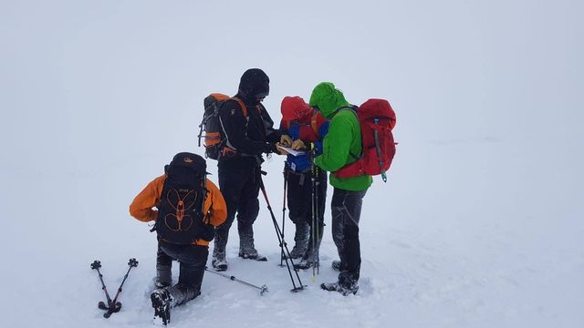 A group gathered around a map on a snowy, misty hillside