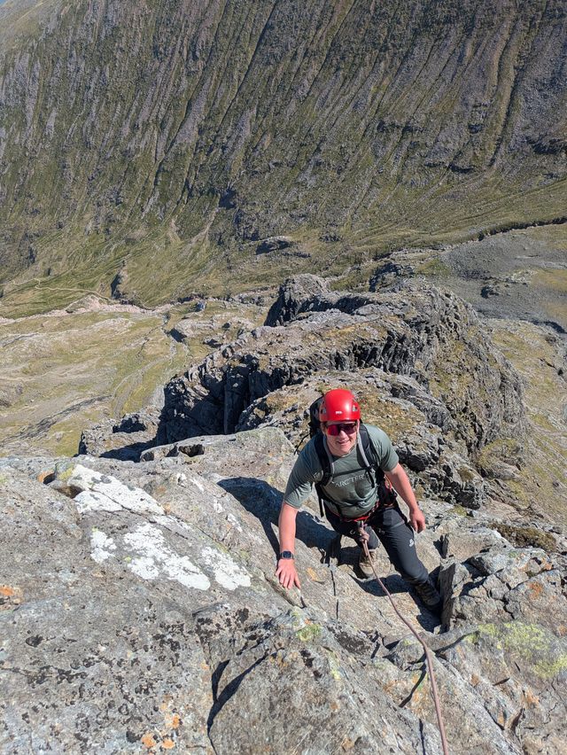 A smiling scrambler in a red helmet climbing a rocky step on Tower Ridge